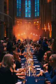 Gasten aan lange dinertafels in de verlichte Gratiekerk tijdens de dinershow.