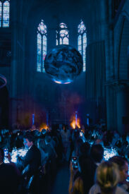 Gasten kijken naar een zwevende wereldbol boven de dinersetting in de Gratiekerk.