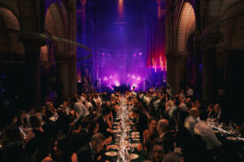 Gasten dineren aan lange tafels in de Gratiekerk met paarse podiumverlichting.